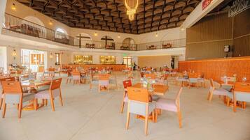 Een ruime hotel eetzaal met meerdere tafels en stoelen, een bar, en een hoog plafond met een geometrisch patroon.