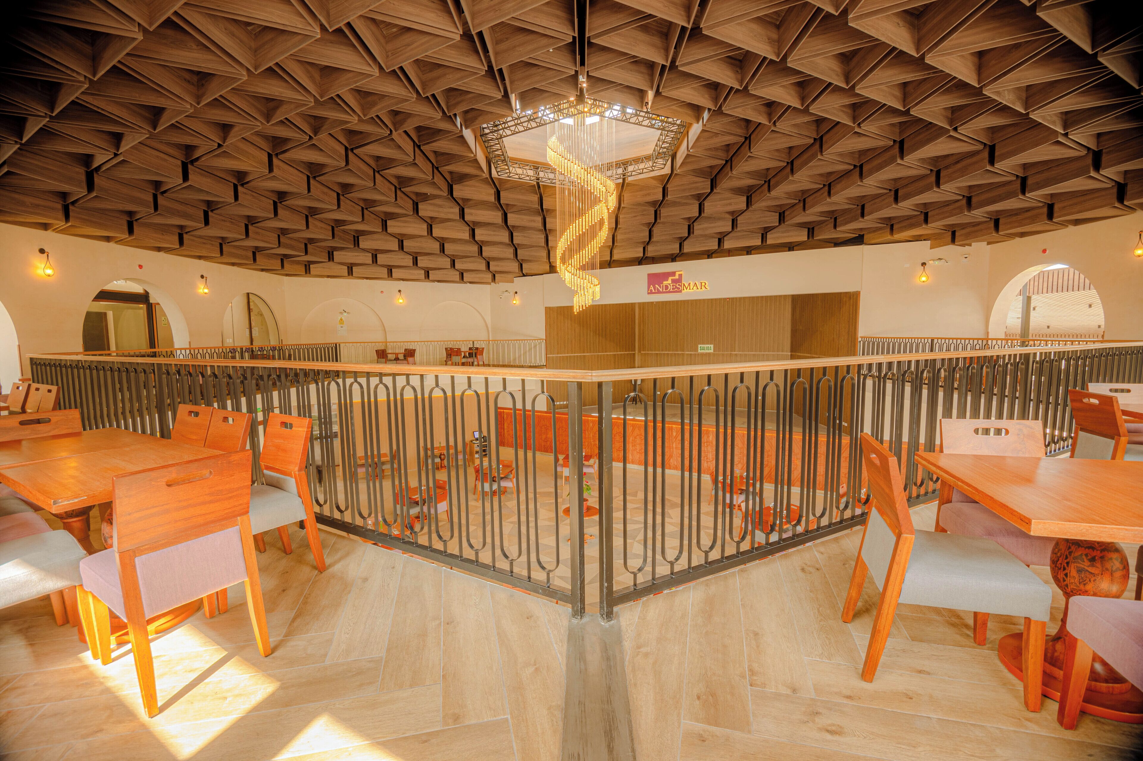 A spacious dining area with wooden tables and chairs, a central decorative light fixture, and a view of the dining area through a glass partition.