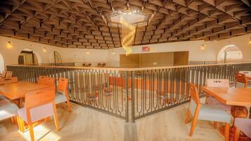 A spacious dining area with wooden tables and chairs, a central decorative light fixture, and a view of the dining area through a glass partition.