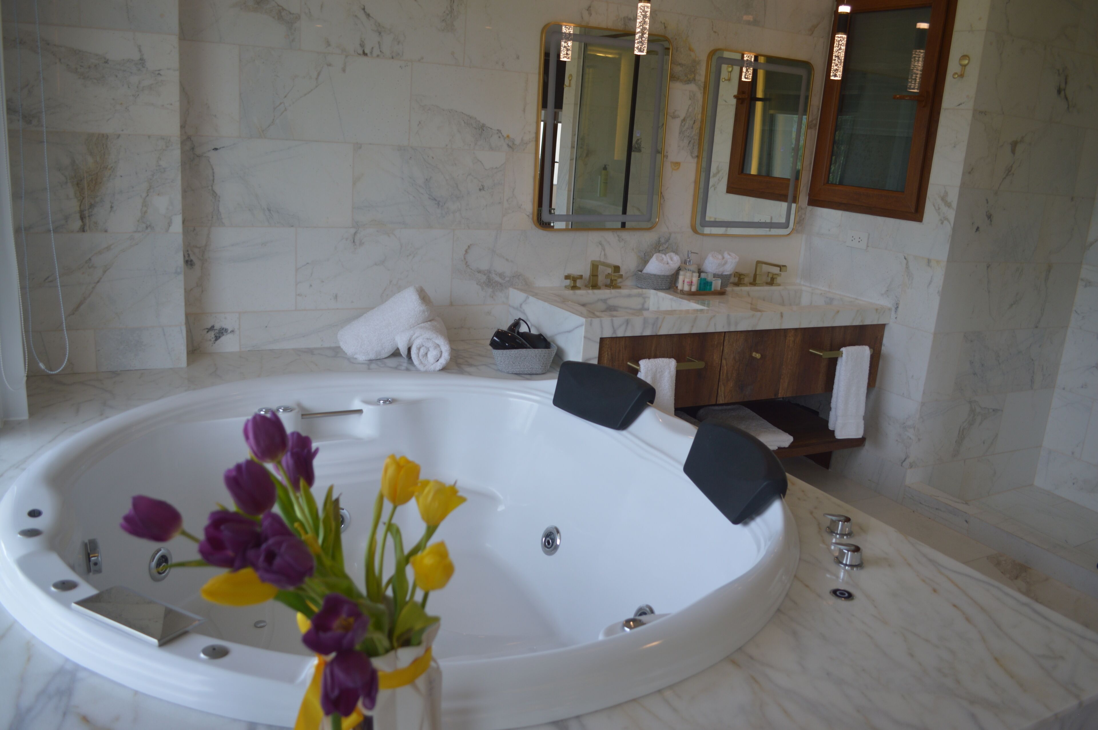 A modern bathroom with a large bathtub, marble walls, two sinks, and a vanity with a mirror.