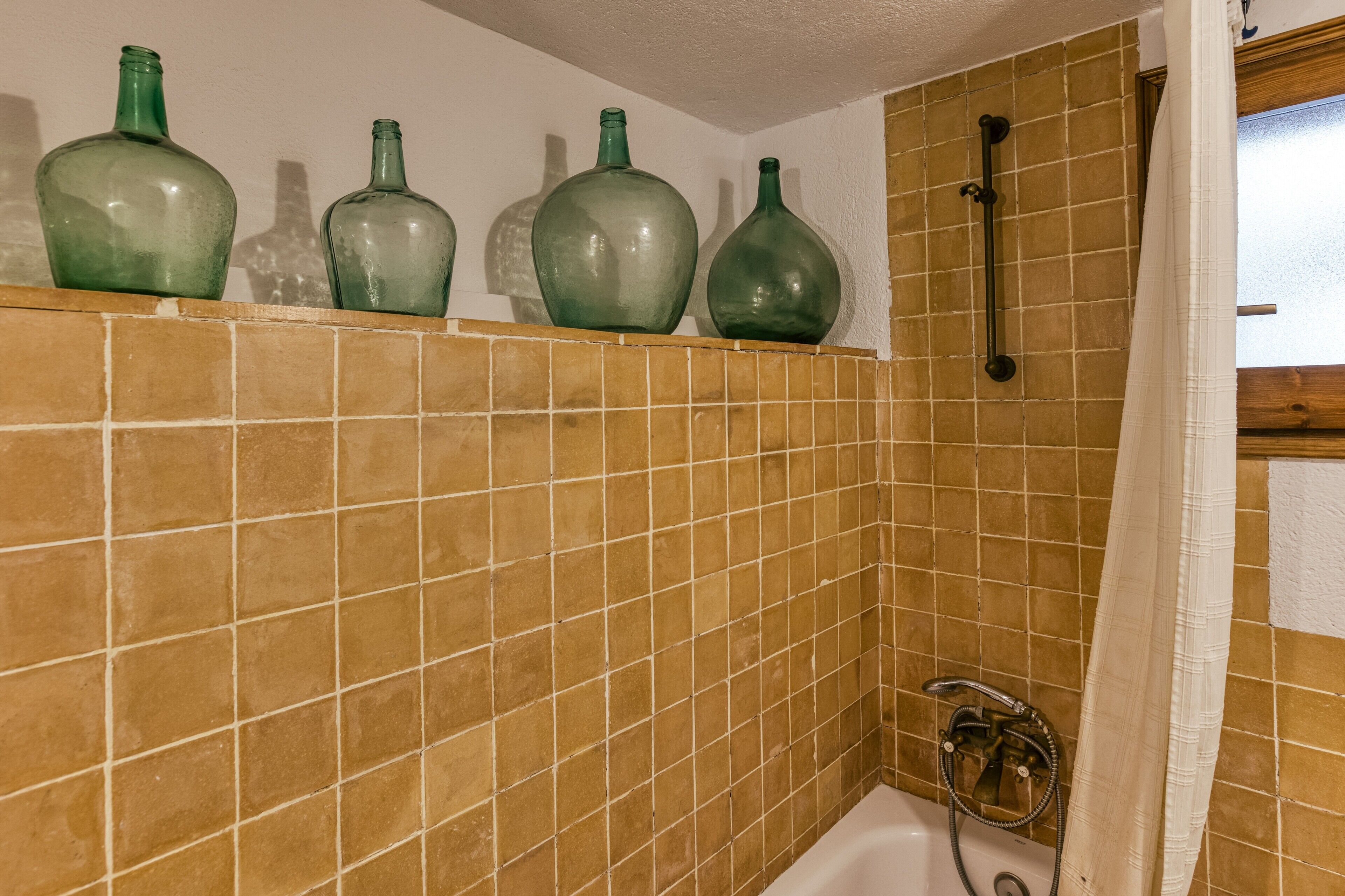 A bathroom with a tiled wall, a shower area, and a shelf with green bottles.