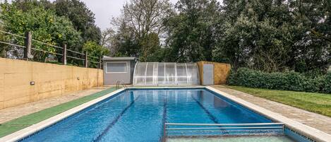 A rectangular swimming pool with clear blue water, surrounded by a concrete deck and a grassy area.