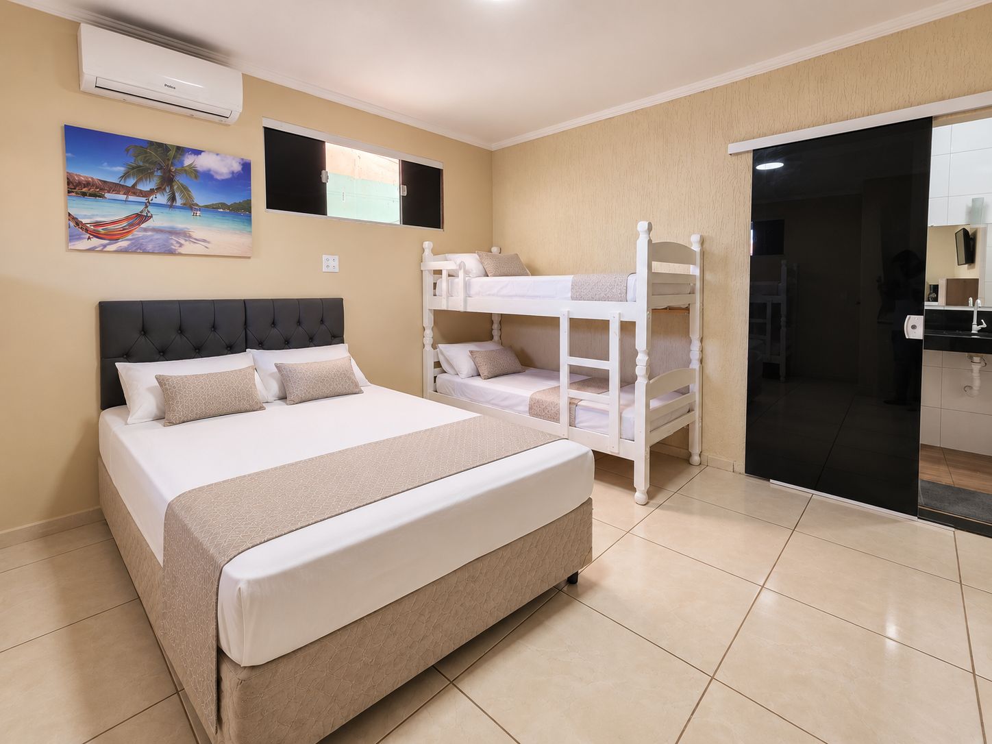 Habitación de hotel con una cama grande, una litera, un cuadro de una playa y una puerta corredera que da al baño.