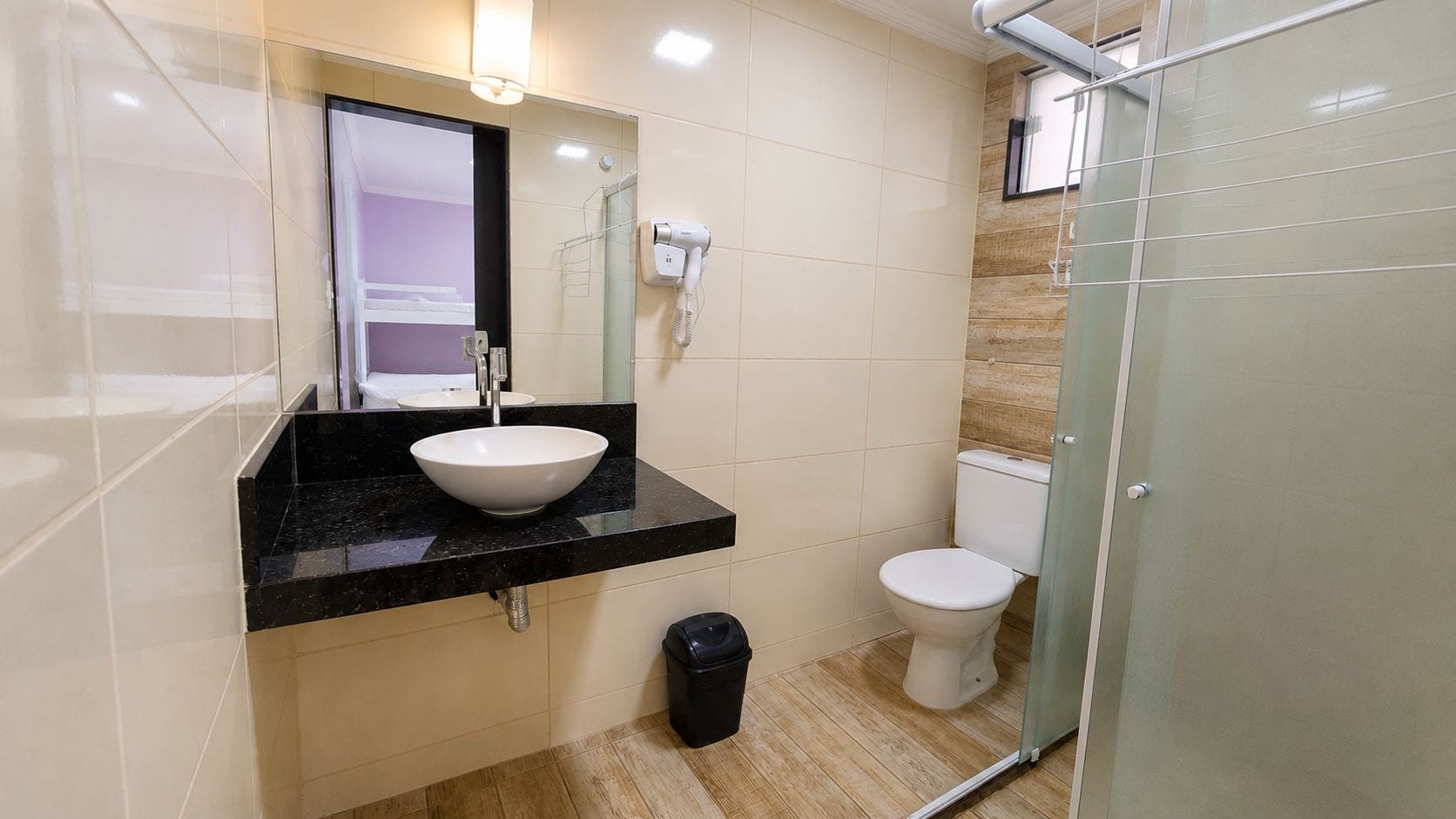 Casa de banho moderna com bancada preta, lavatório branco e cabine de duche em vidro.
