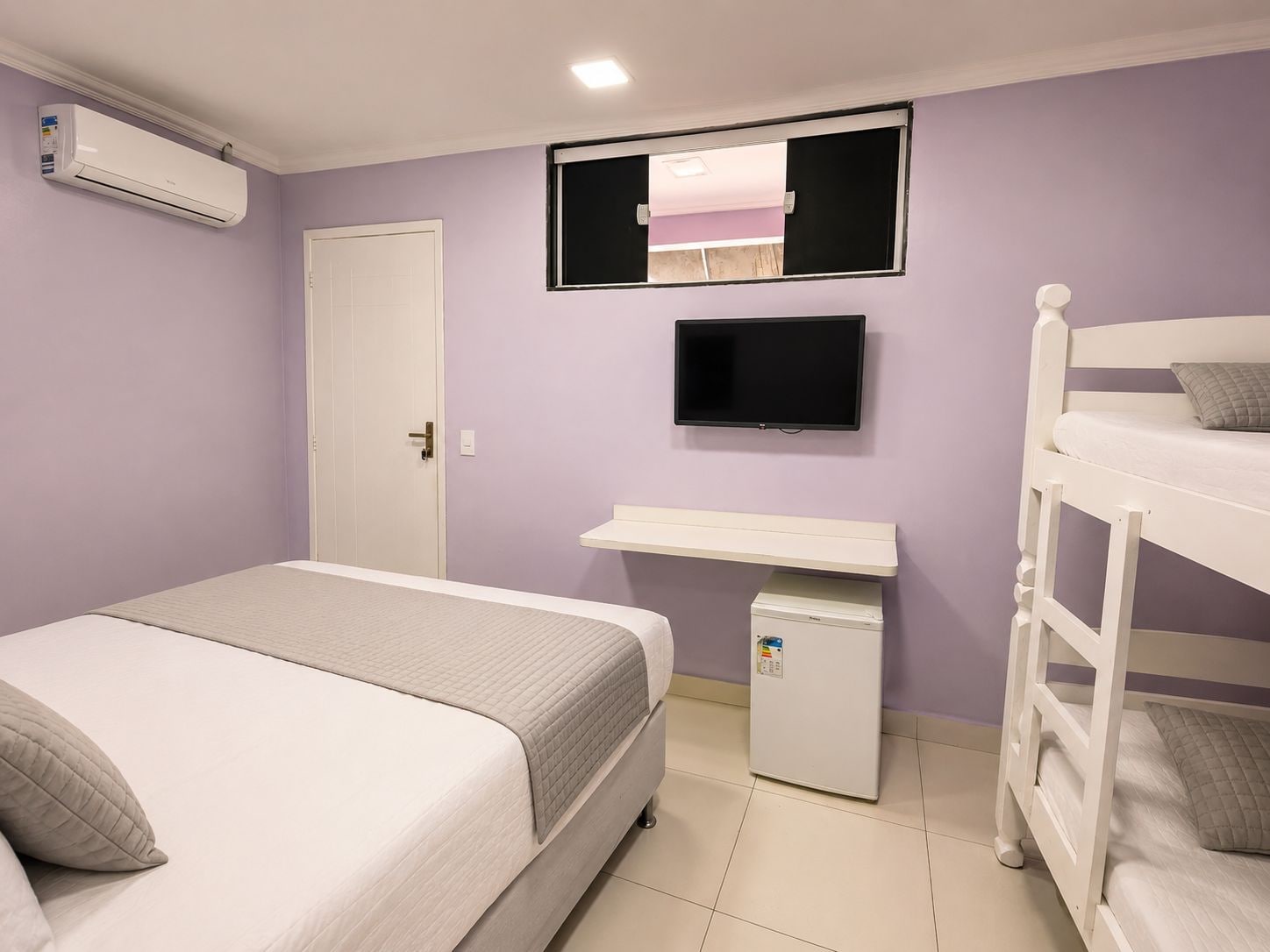 A bedroom with a bed, a TV, a small fridge, and a bunk bed.