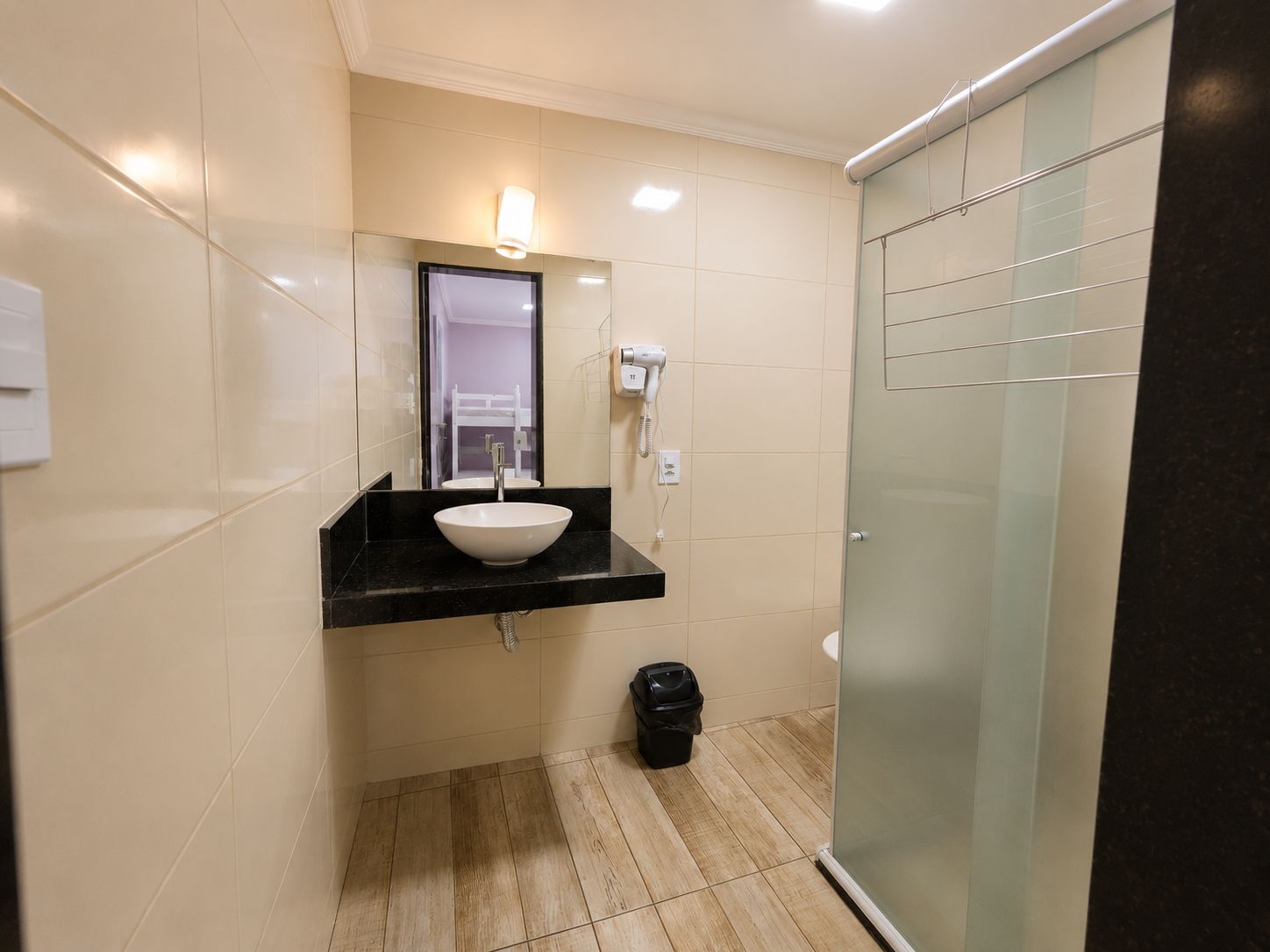 Un baño con lavamanos blanco, un espejo, secador de pelo y zona de ducha.