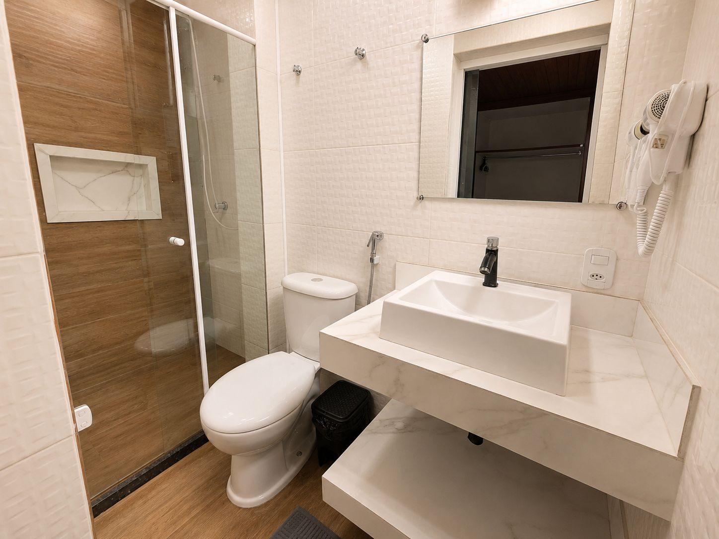A modern bathroom with a glass shower enclosure, a white toilet, a sink with a mirror above it, and a towel rack.