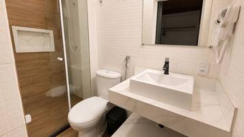 A modern bathroom with a glass shower enclosure, a white toilet, a sink with a mirror above it, and a towel rack.