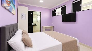 Une chambre à coucher avec un lit, une table de chevet, un téléviseur et une salle de bain visible à travers une porte ouverte.