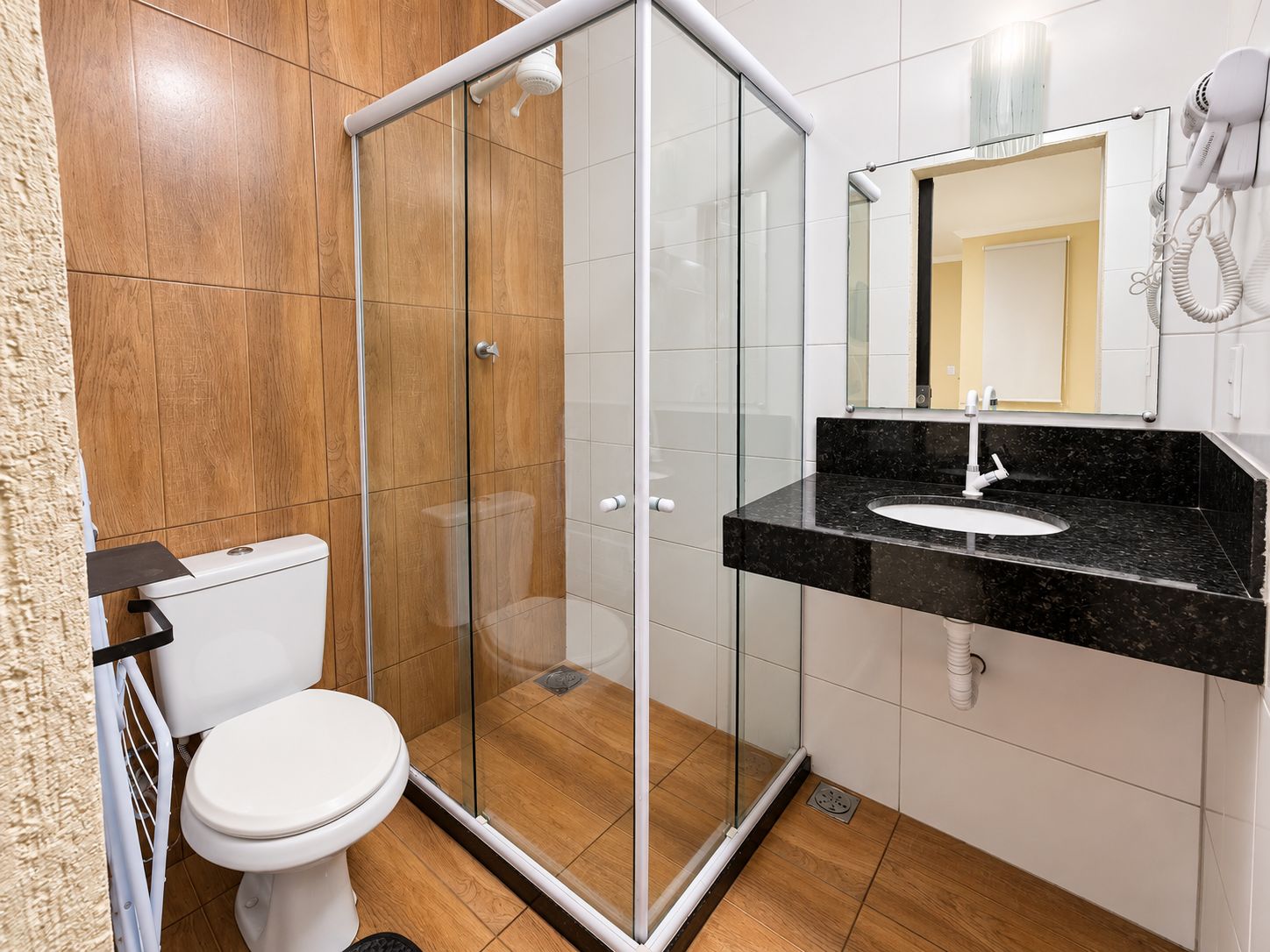 Un baño moderno con ducha envuelta en vidrio, inodoro blanco y lavamanos de mármol negro.