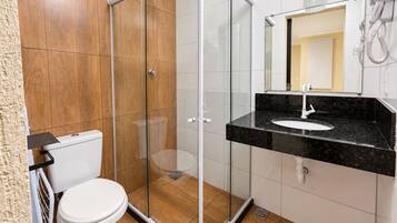 Un baño moderno con ducha envuelta en vidrio, inodoro blanco y lavamanos de mármol negro.
