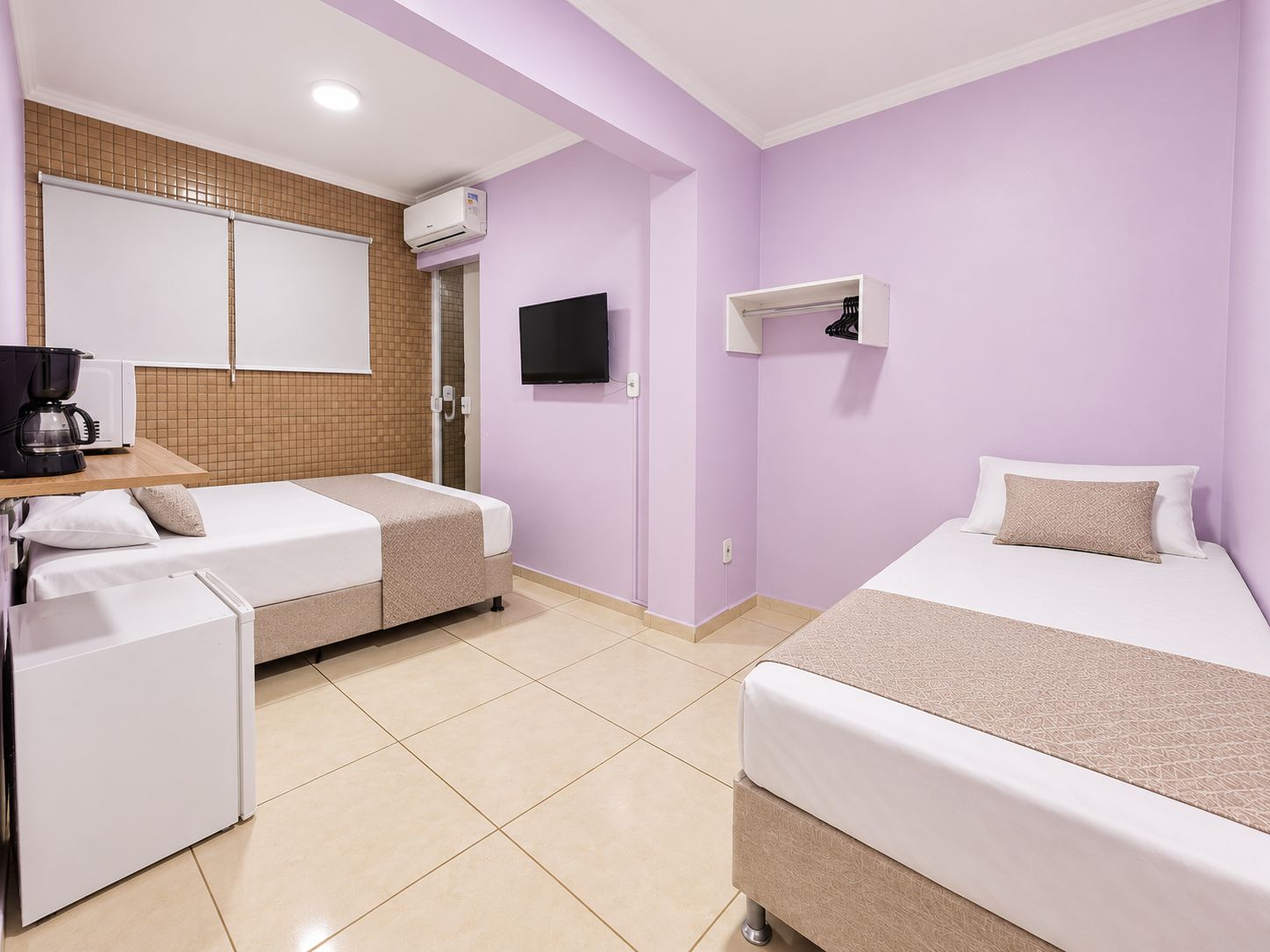 A hotel room with two beds, a TV, a coffee maker, and a small kitchenette.