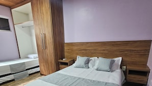 A neatly made bed with a quilted cover, wooden headboard, and bedside tables with lamps. - Alice Suites (Arraial do Cabo)