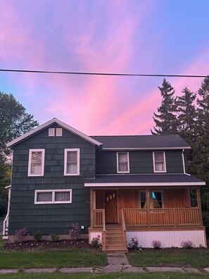 A two-story house with a front porch and a small garden. - Spacious 5-bedroom house, WiFi, AC, 1 block from Lake & Main St. (Sterling)