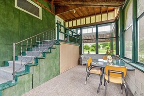 Ein Zimmer mit Treppe, Tisch mit Stühlen und großen Fenstern mit Blick auf viel Grün.