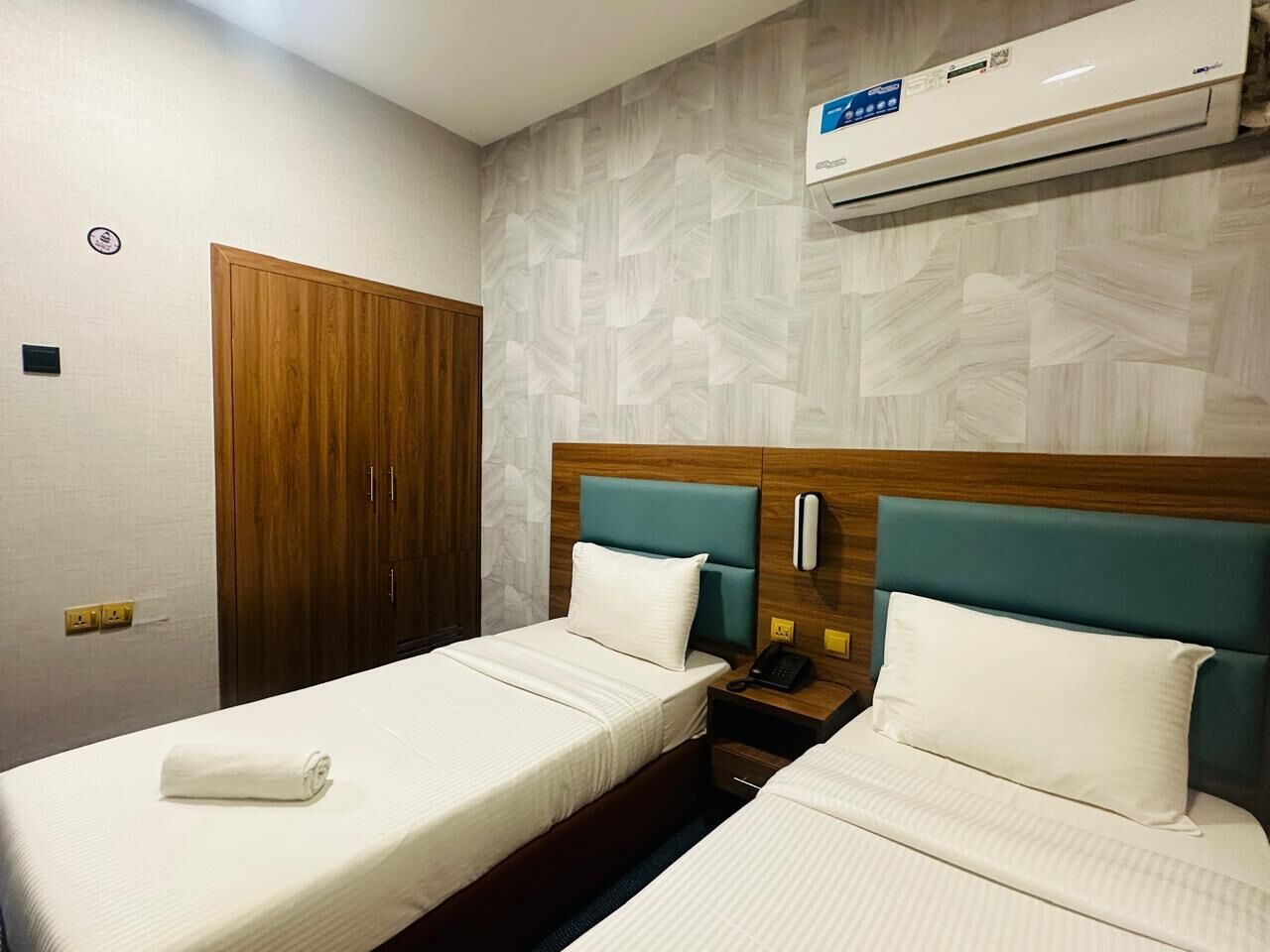 A hotel room with two beds, wooden headboards, a wall-mounted air conditioner, and a wooden wardrobe.
