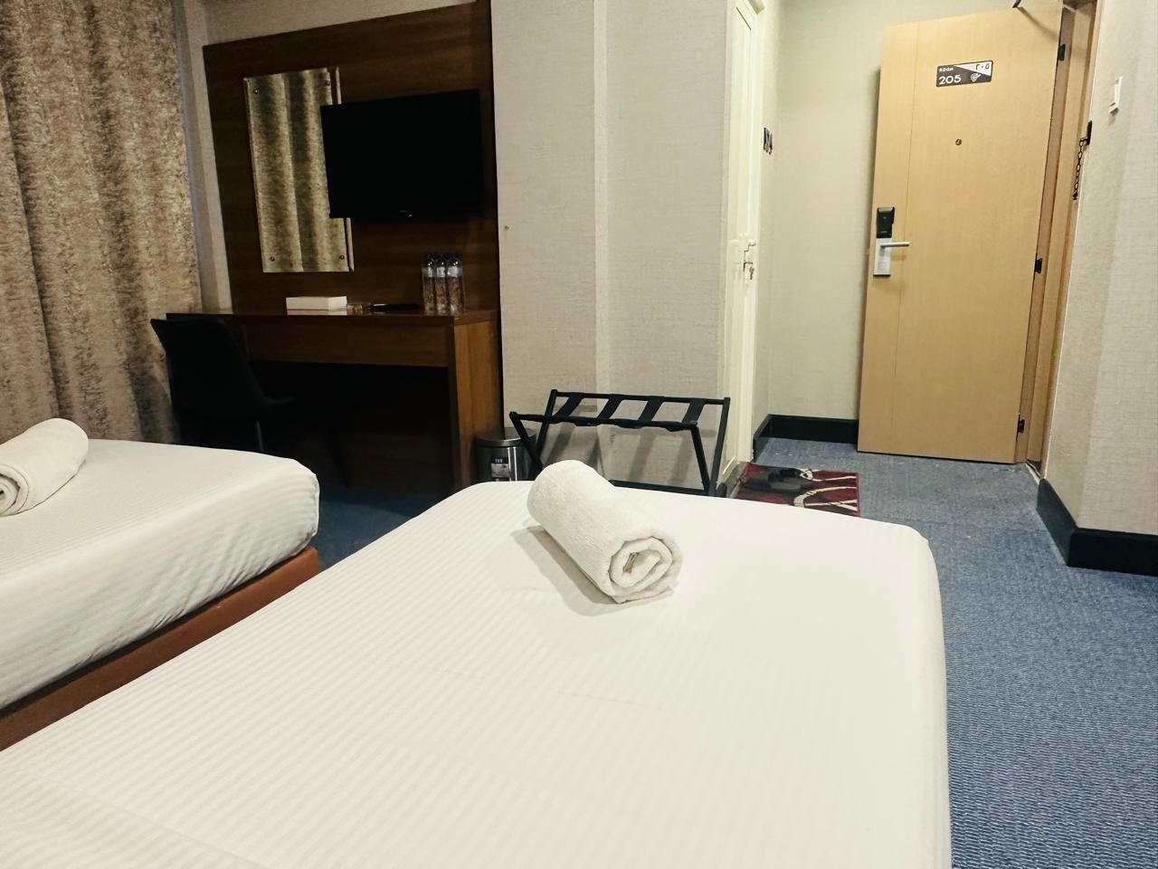 A hotel room with two beds, a desk, a TV, and a door marked "205".