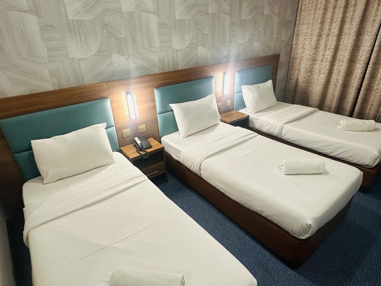A hotel room with three single beds, each with a wooden headboard, white linens, and bedside tables with lamps.