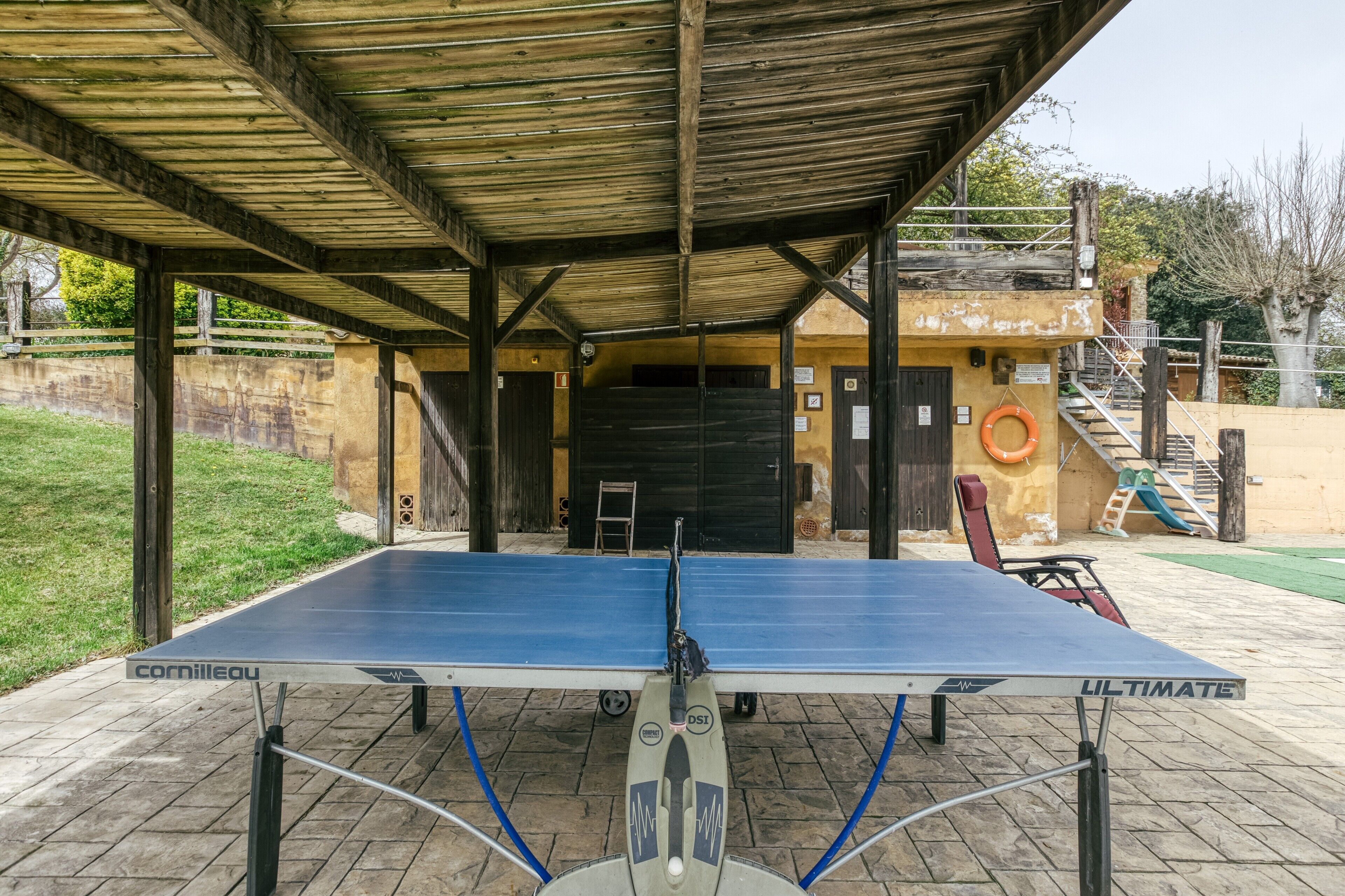 A ping pong table under a wooden shelter with a wall and a door in the background.