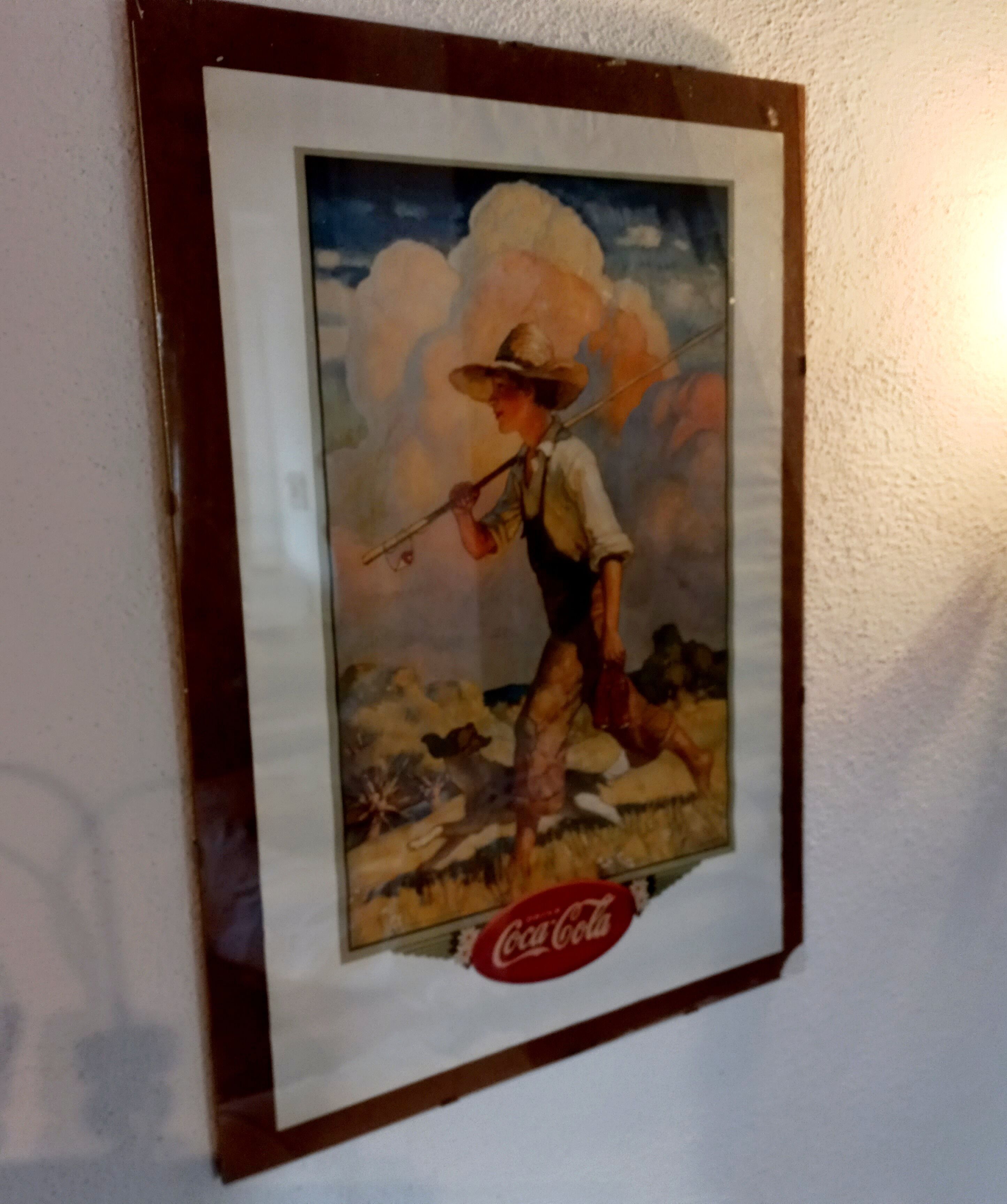 Et indrammet billede af en mand i hat og overalls, der holder et gevær, med Coca-Cola logo i bunden.
