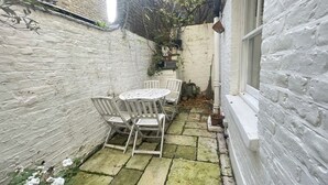 A small patio with a round table and chairs, surrounded by white brick walls and a stone floor. - Second nest Chelsea (London)