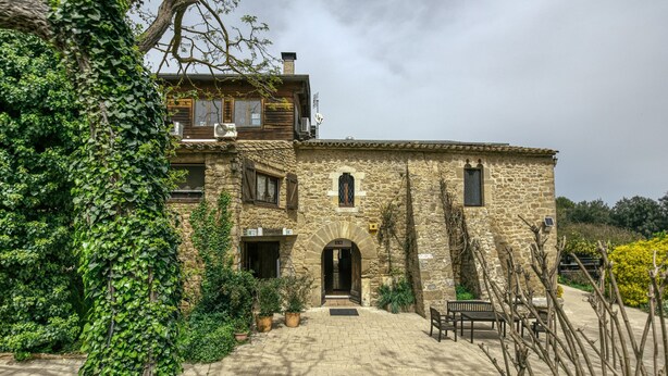 A stone building with a wooden upper level, a paved courtyard, and potted plants. - Room 'Tramuntana' with Shared Pool, Wi-Fi and Air Conditioning (Girona)