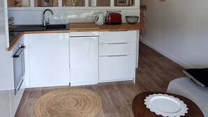 Una cucina moderna con mobili bianchi, un piano di lavoro in legno, un lavello e un'ampia finestra. Sopra il bancone, una lampada a soffitto intrecciata.