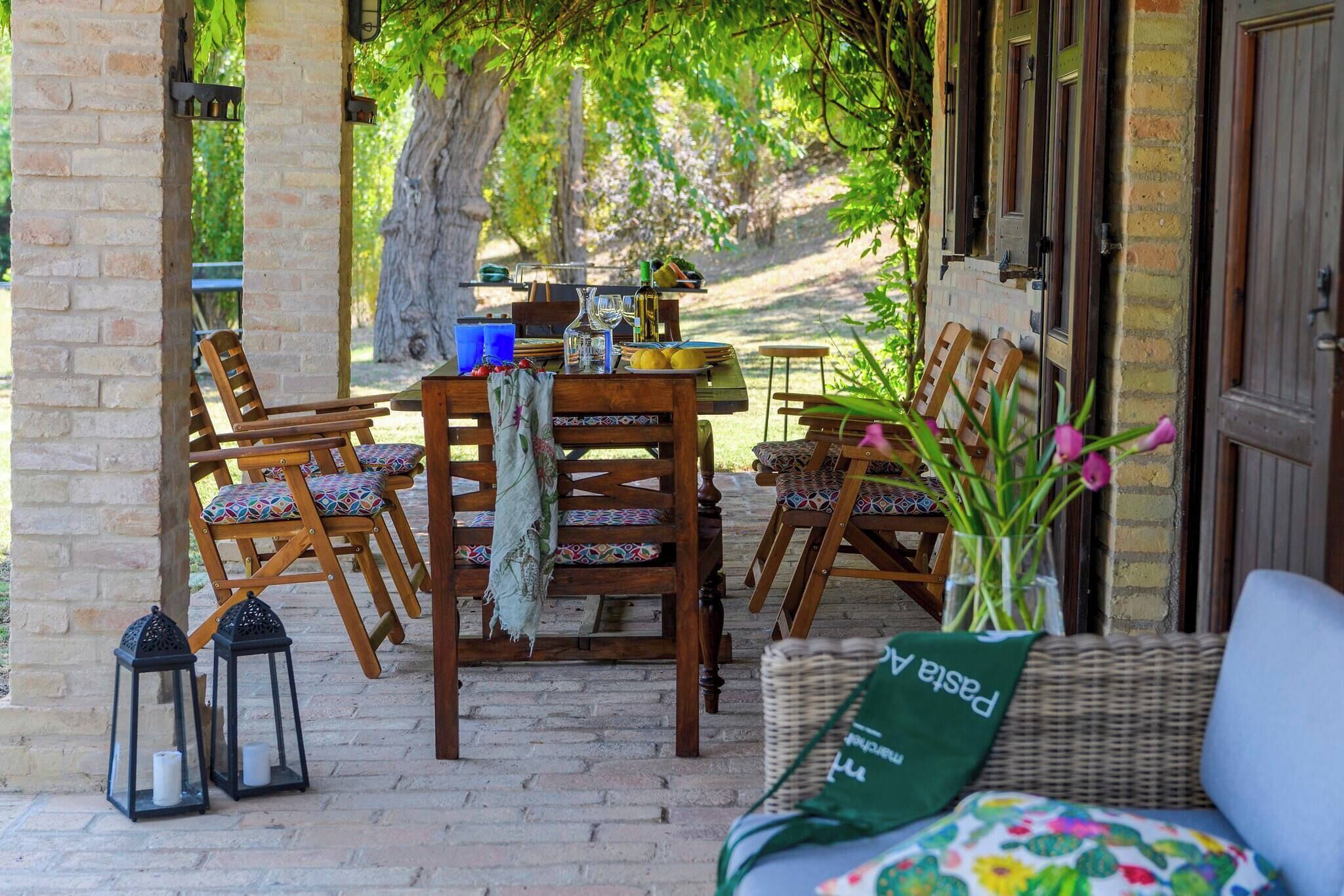 Un espace extérieur abrité, aménagé pour les repas, avec des chaises en bois et une table dressée.