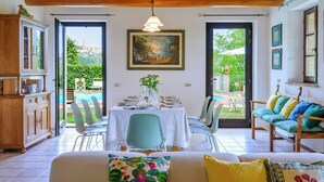 Ein Essbereich mit Tisch für vier Personen, einer Couch und Blick auf Pool und Grünflächen.