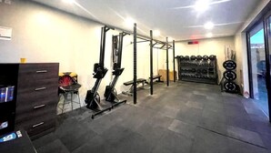 Une salle de sport à domicile équipée d’une barre de traction, d’un banc de musculation et de divers poids.
