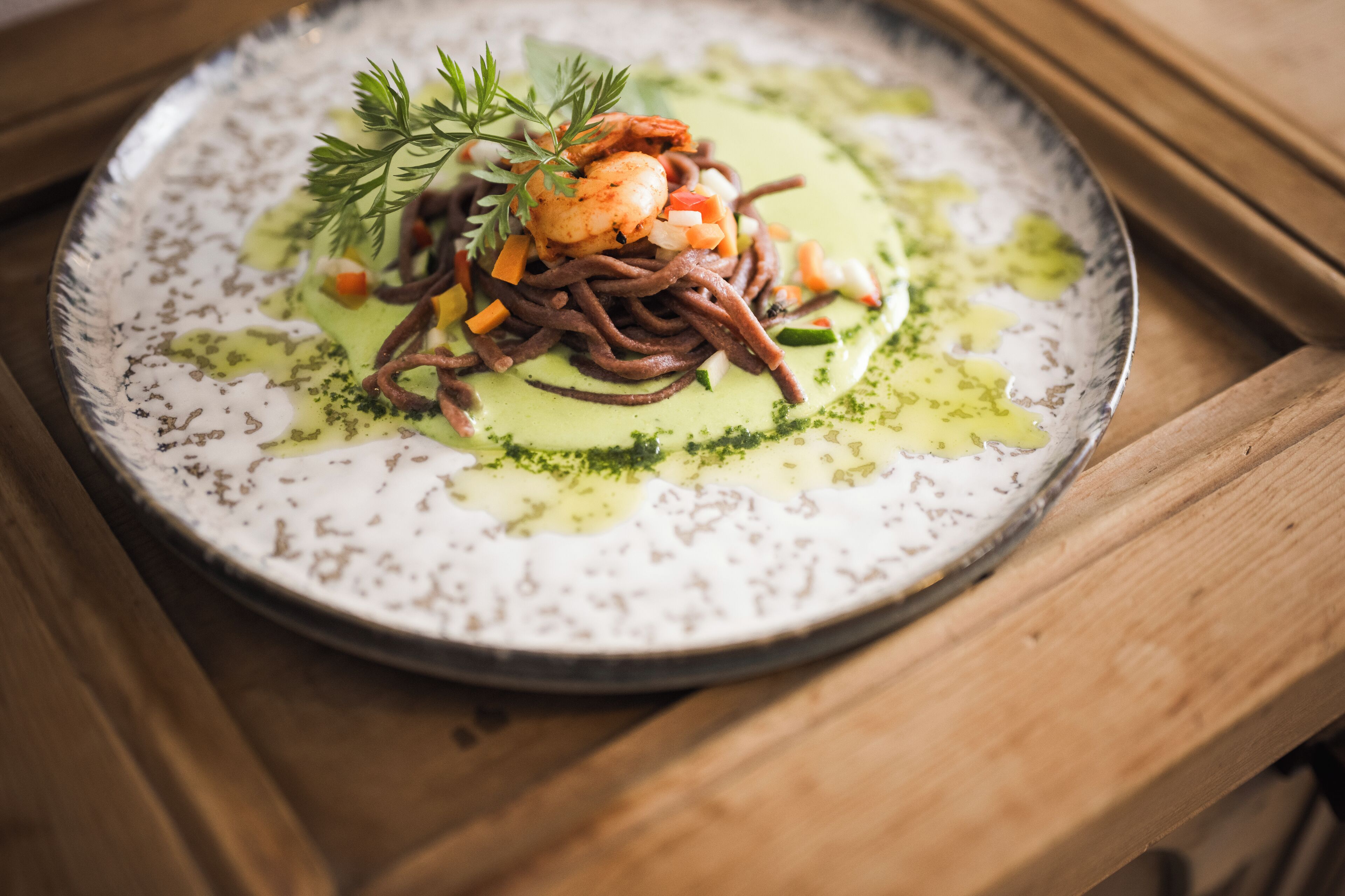A plate of food with a green sauce, shrimp, and vegetables on a speckled plate.