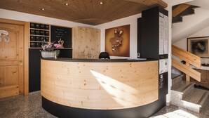 Un comptoir d’accueil avec un revêtement en bois, un tableau noir indiquant les numéros des chambres et un escalier avec une rampe en bois.