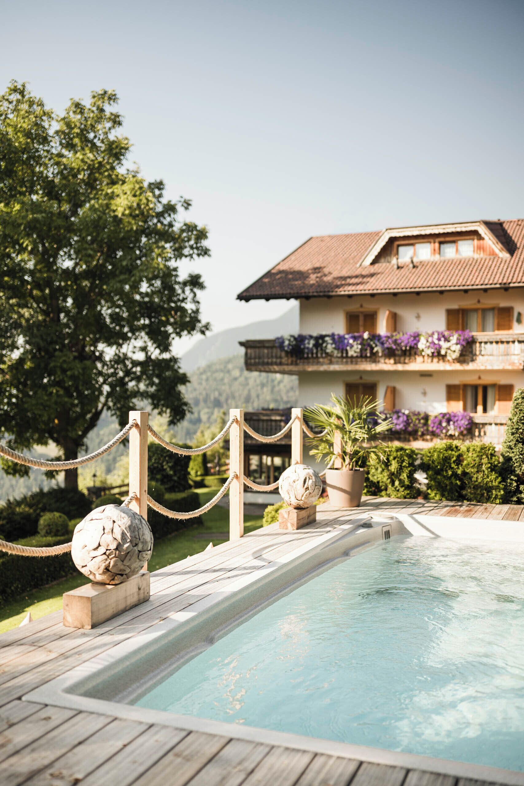 Un espace piscine doté d’une terrasse en bois, d’une barrière en corde et d’une sculpture en pierre.