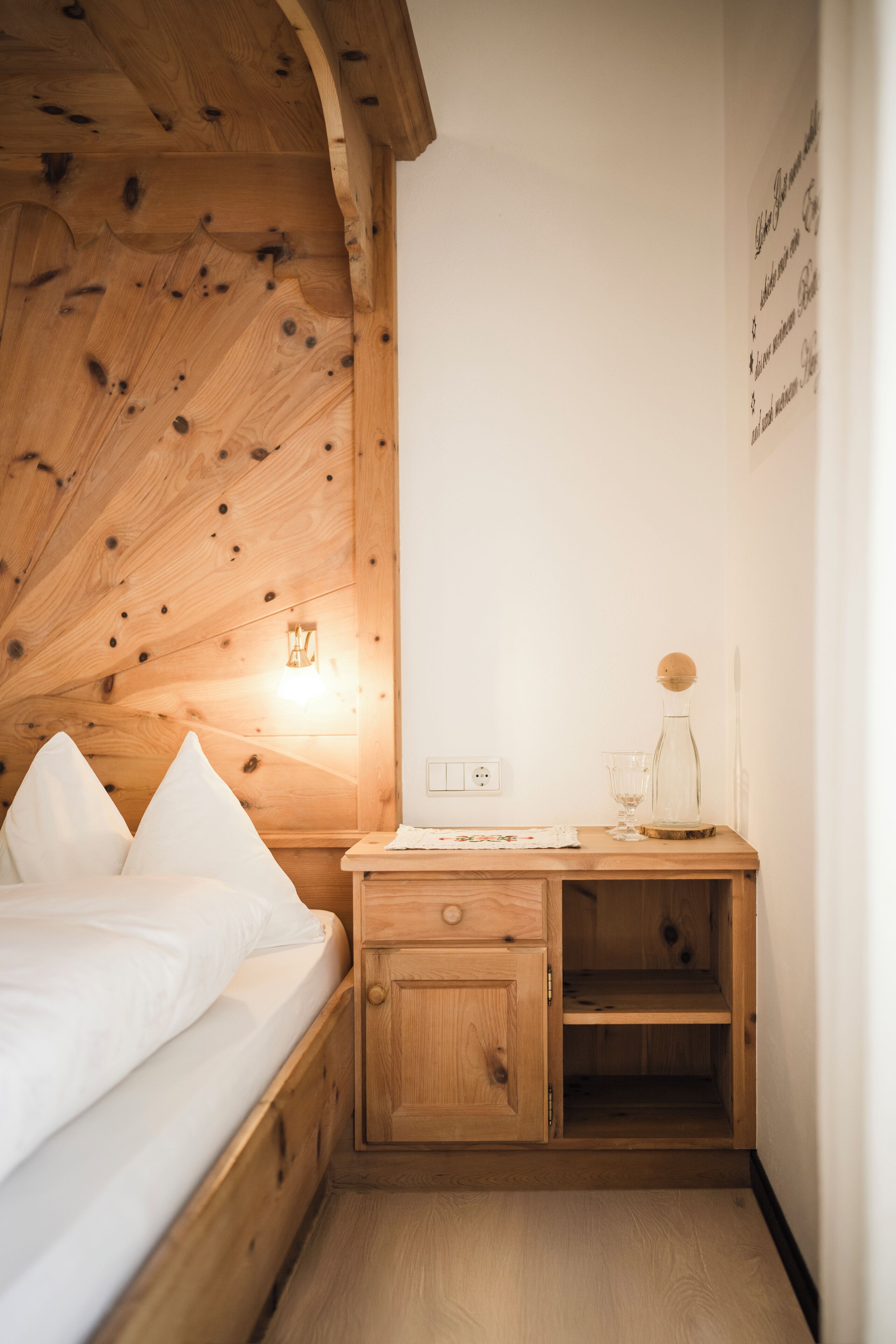 Ein Zimmer mit Holzboden, einem Bett, einem Nachttisch, einer Wandleuchte und einem kleinen Schrank.