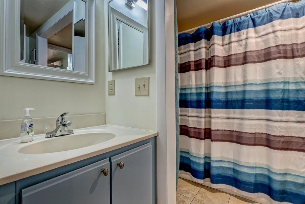 Un baño con un lavabo blanco, un espejo y una cortina de ducha a rayas.