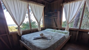 A wooden cabin bedroom with a bed, curtains, and a view of the outdoors.