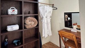 Een kamer met een houten garderobe, een badjas aan een rek, een houten tafel met stoelen, en een spiegel aan de muur.