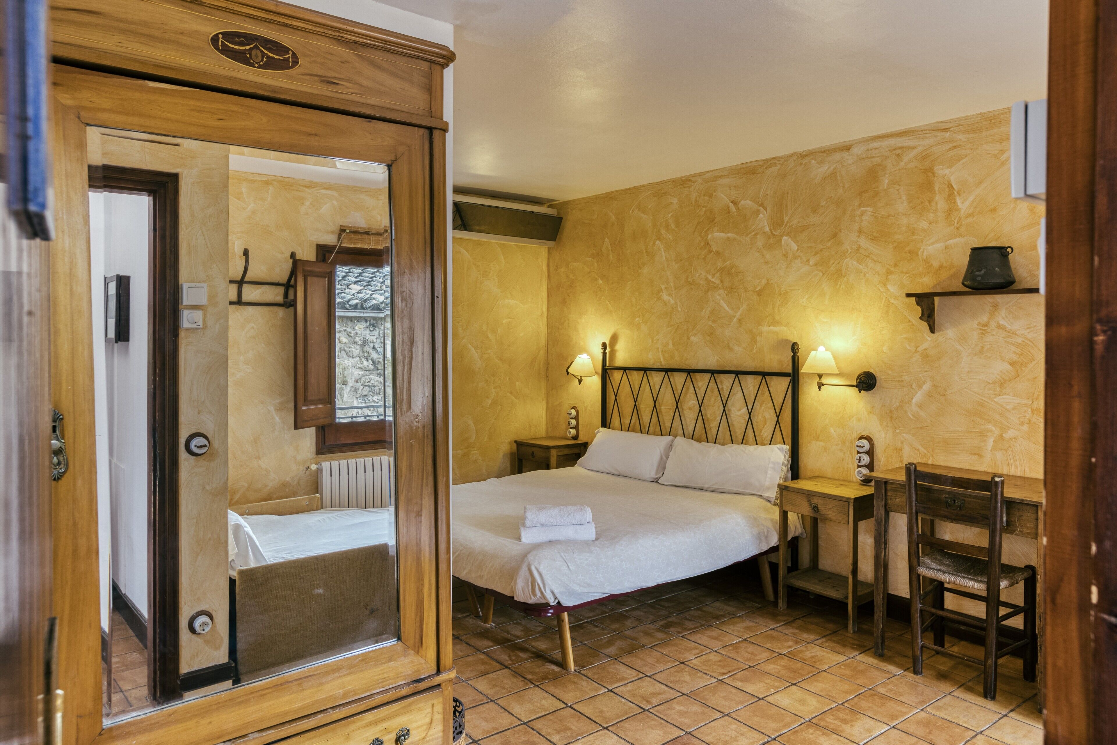 Een slaapkamer met een bed, een houten garderobe, een tafeltje en een stoel.