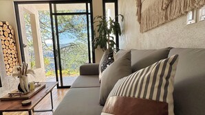 Een moderne woonkamer met een modulaire bank, een macramé wanddecoratie en uitzicht op het landschap door grote schuifdeuren.