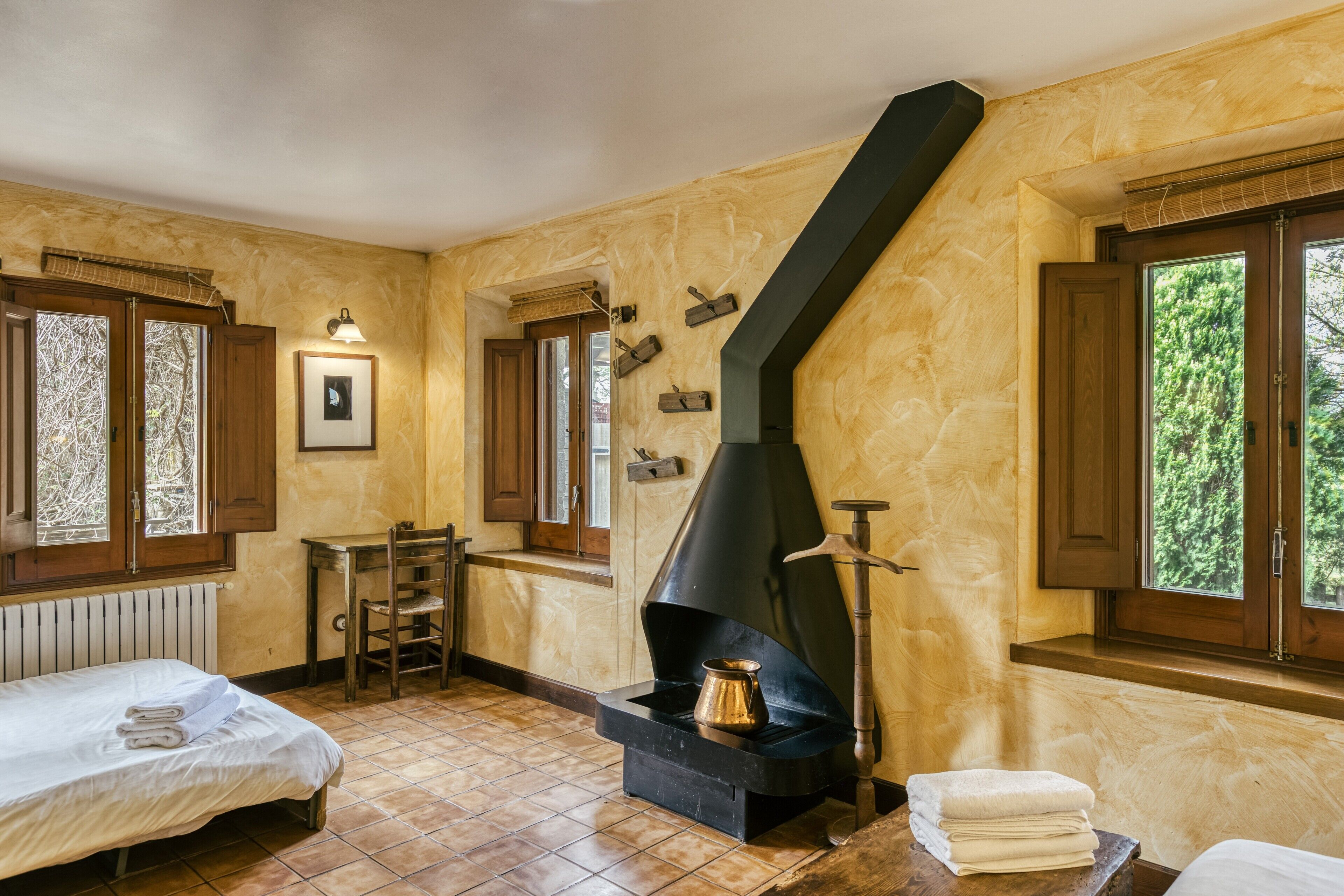 Una habitación con chimenea, una cama, una silla y una ventana con vistas a árboles.