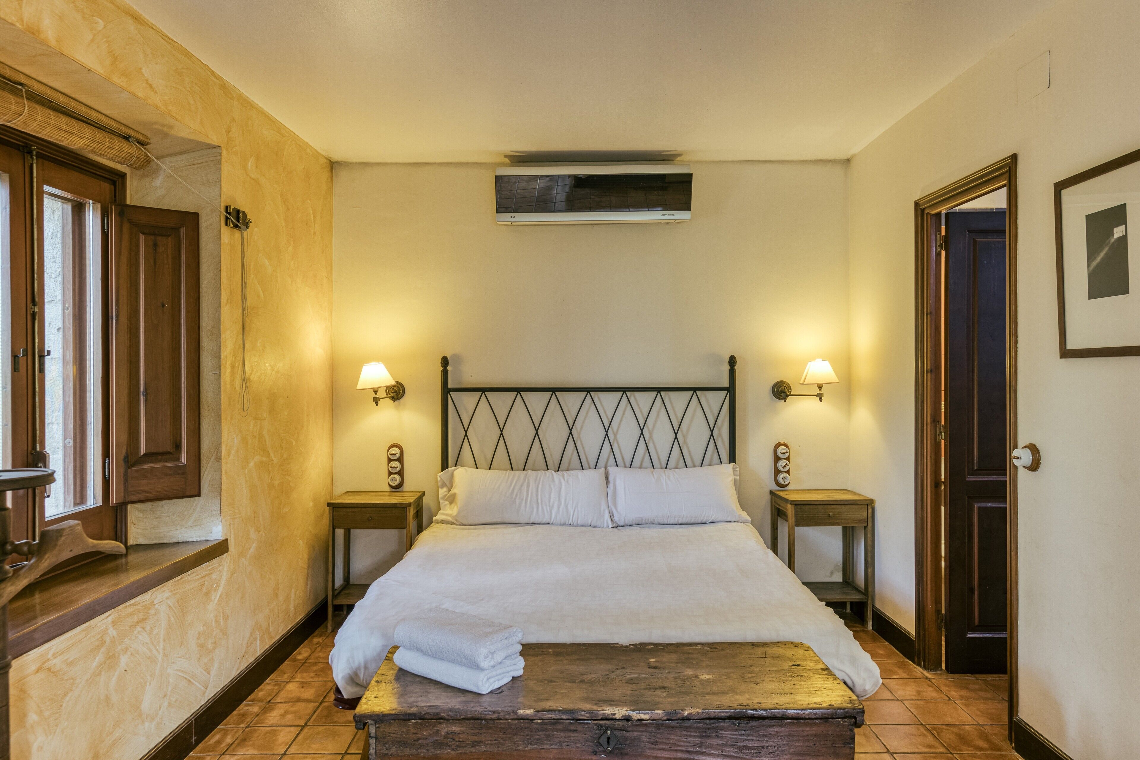 A hotel room with a bed, two bedside tables, a wall-mounted air conditioner, and a door.