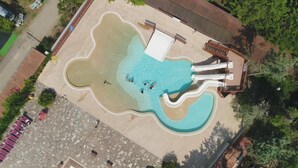 Oversigtsbillede af en swimmingpool med rutsjebane, omgivet af en terrassedæk med siddepladser og et mindre bassin.