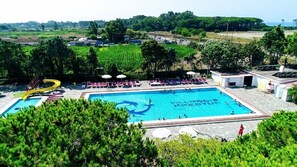 Une piscine avec un toboggan jaune, entourée de chaises longues et de parasols.