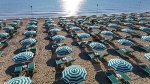 Ein Strand mit Reihen von Liegestühlen und gestreiften Sonnenschirmen.