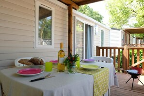 A dining table set outdoors with a white tablecloth, plates, cutlery, a bottle, and a decorative plant.