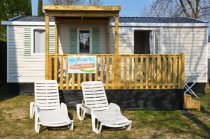 A mobile home with two white plastic lounge chairs in front, a wooden deck, and a sign that reads "Happy Premium."