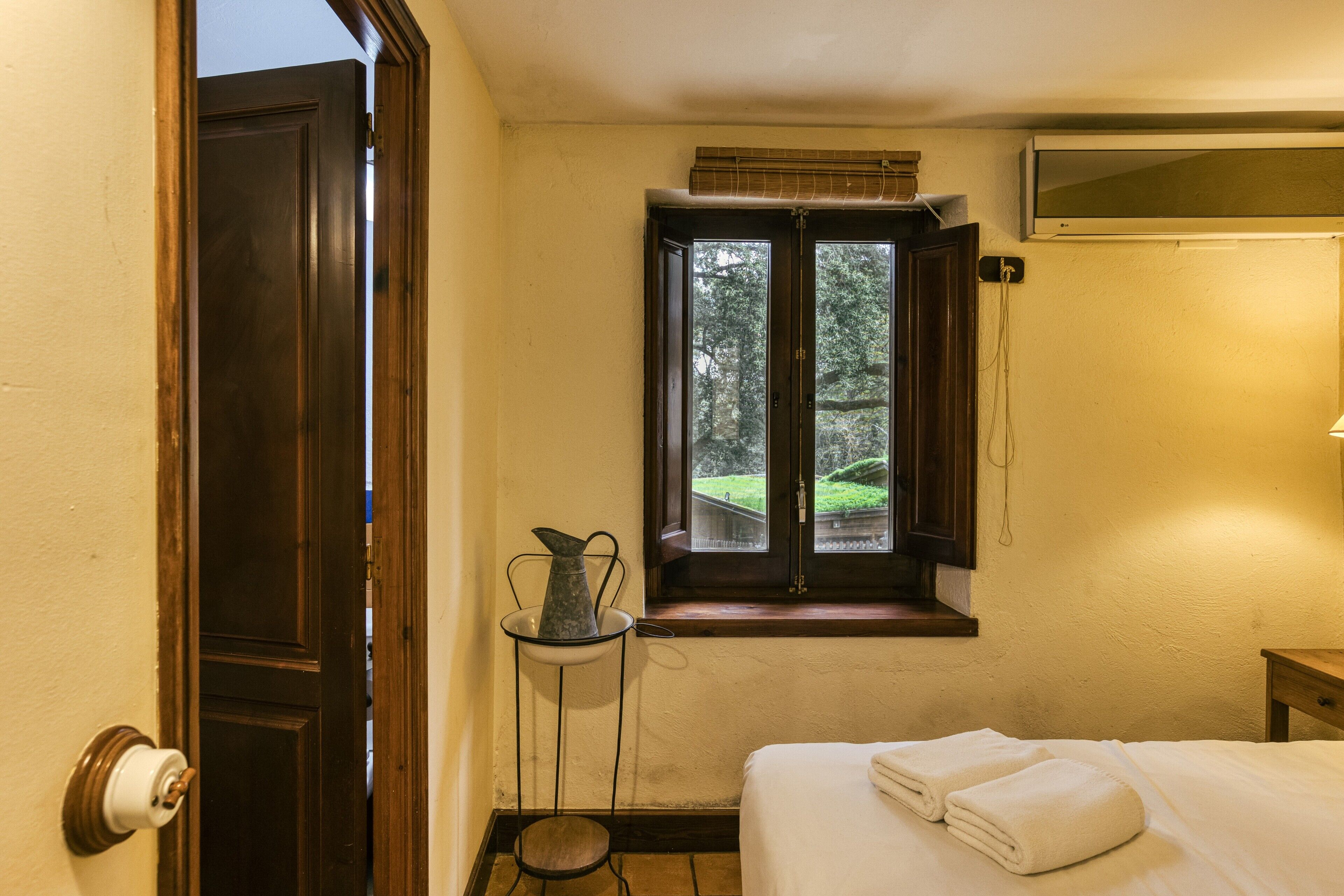A bedroom with a bed, a window with a view, a bedside table, and a door.