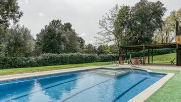 Una piscina rectangular con un trampolín, rodeada de césped y árboles.