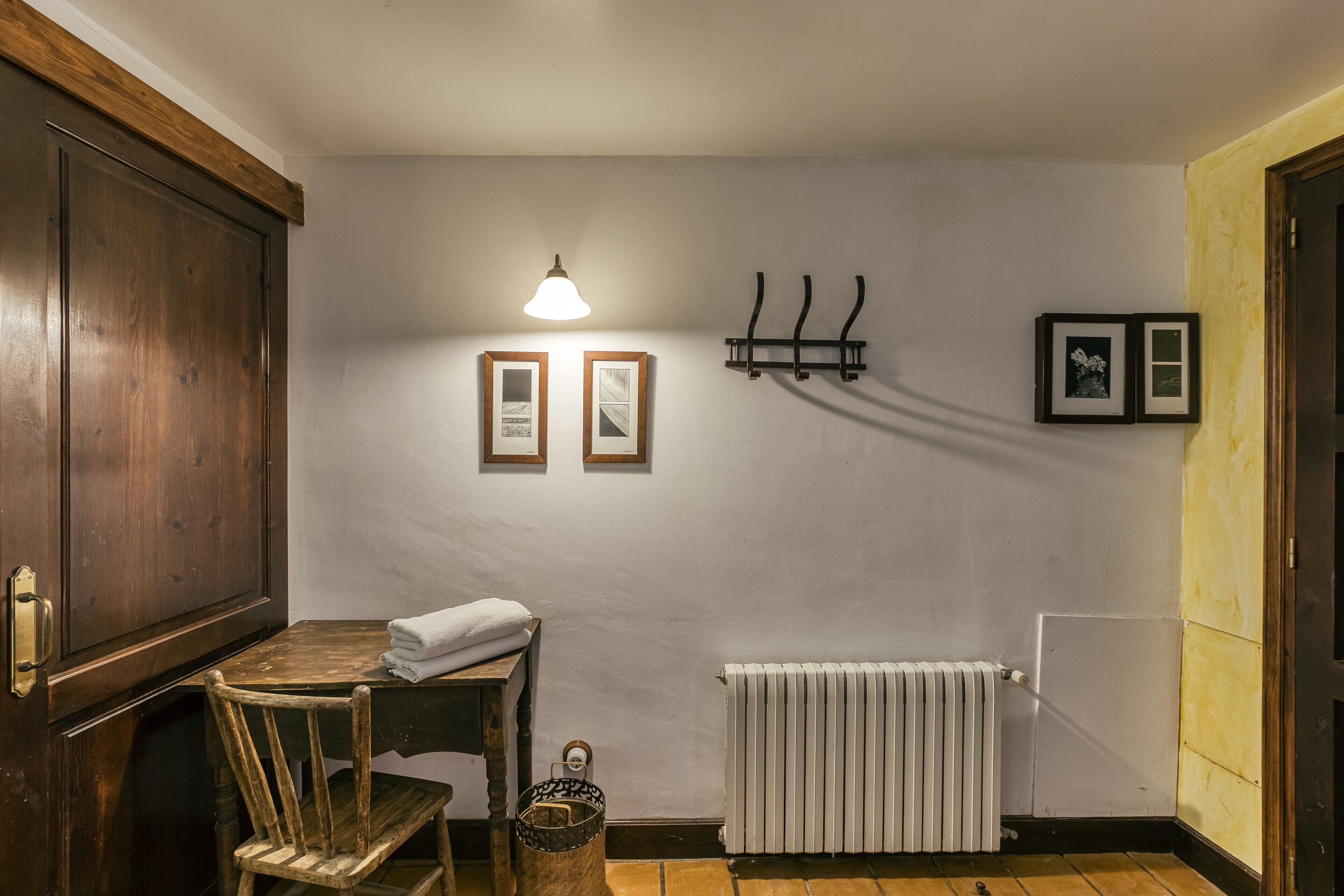 A room with a wooden table, a chair, a radiator, and wall-mounted pictures.