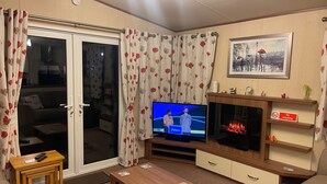 Ein Wohnzimmer mit Fernseher, Kamin, Sofa, Couchtisch und einem kleinen Tisch mit Fernbedienung.